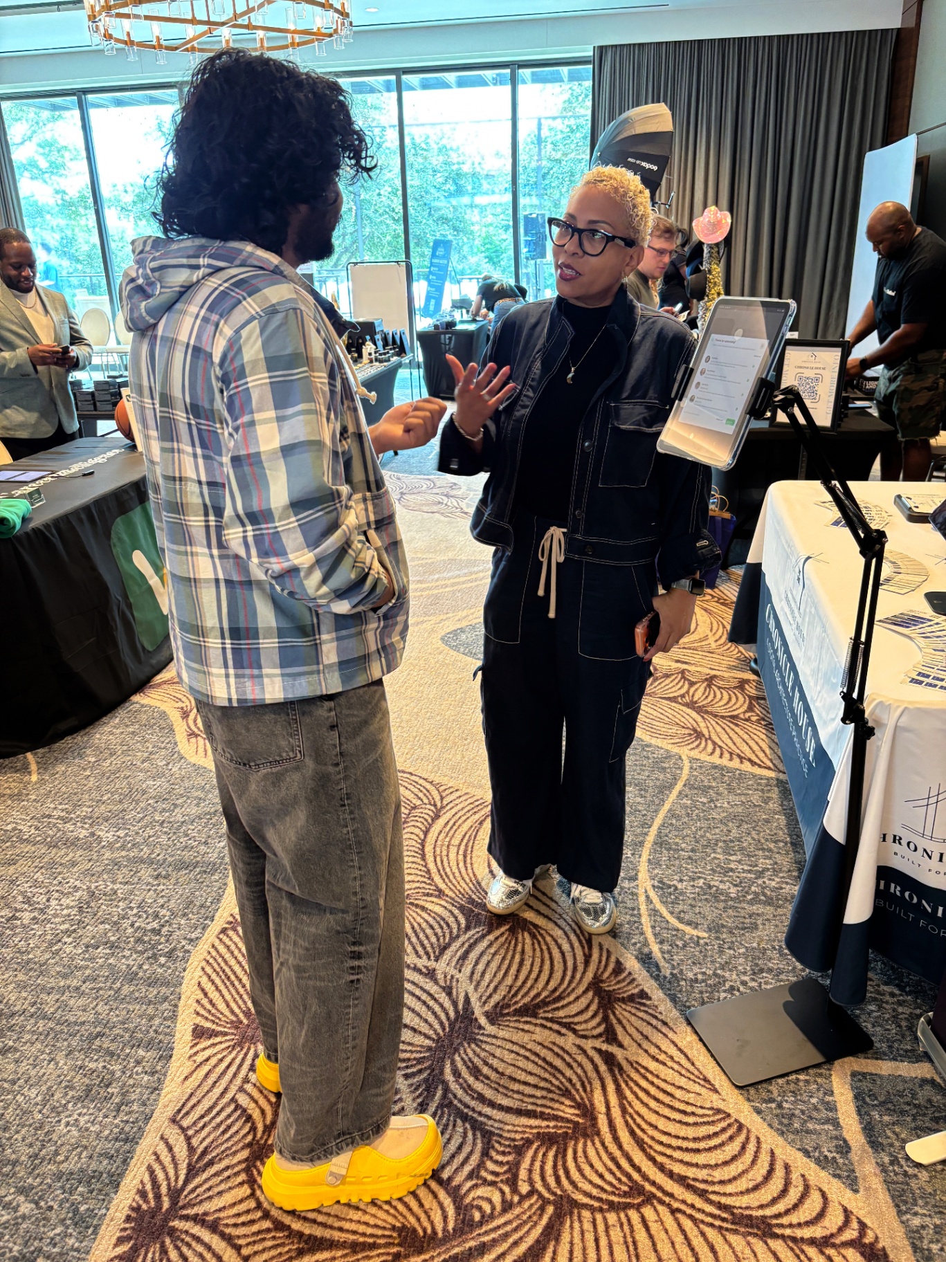 Founder talking with an attendee in front of the Chronicle House booth, tablet kiosk visible.
