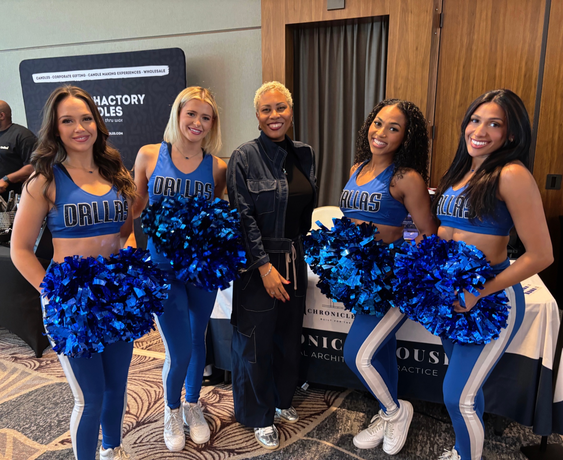 Founder posing with four Dallas Mavericks Dancers in front of the Chronicle House booth.