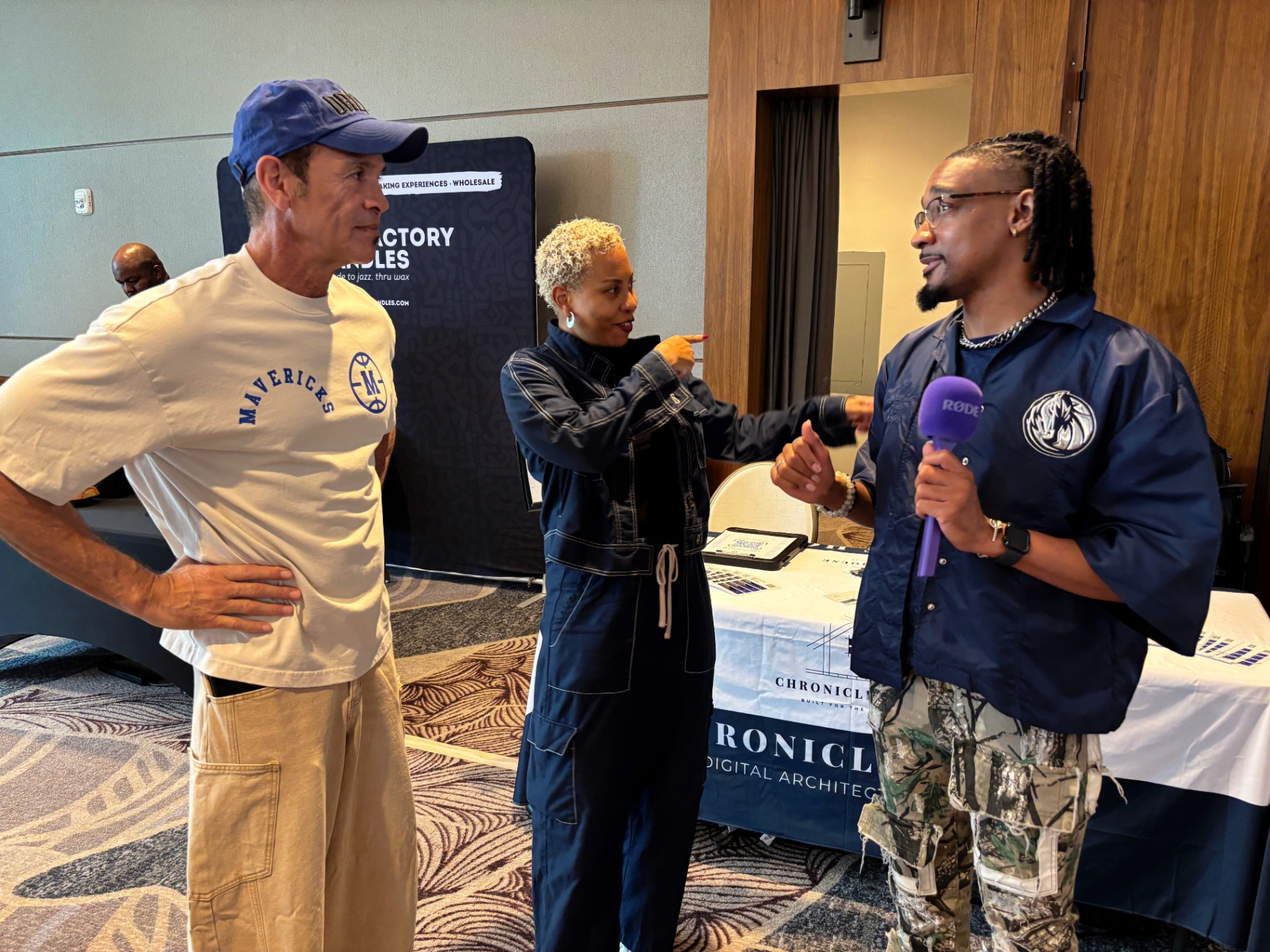 Founder mid-conversation with a Mavericks team member and a host holding a Rode microphone in front of the Chronicle House booth.